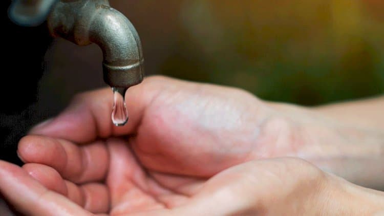 Grifo con una gota de agua cayendo sobre manos