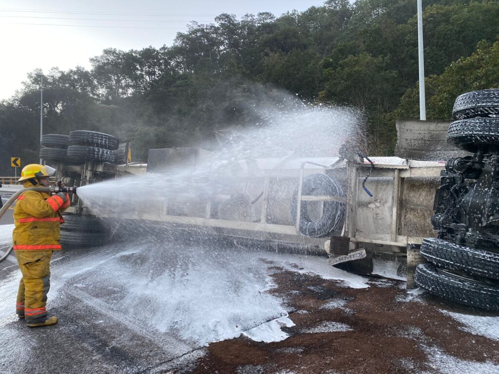 Elemento de bomberos con una manguera con agua apagando el fuego de un remolque de un tráiler con gasolina en la autopista Durango-Mazatlán tras un accidente tipo volcadura