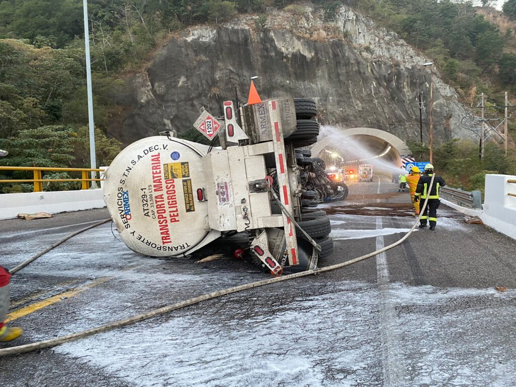 Elementos de bomberos con una manguera con agua apagando el fuego de un remolque de un tráiler con gasolina en la autopista Durango-Mazatlán tras un accidente tipo volcadura