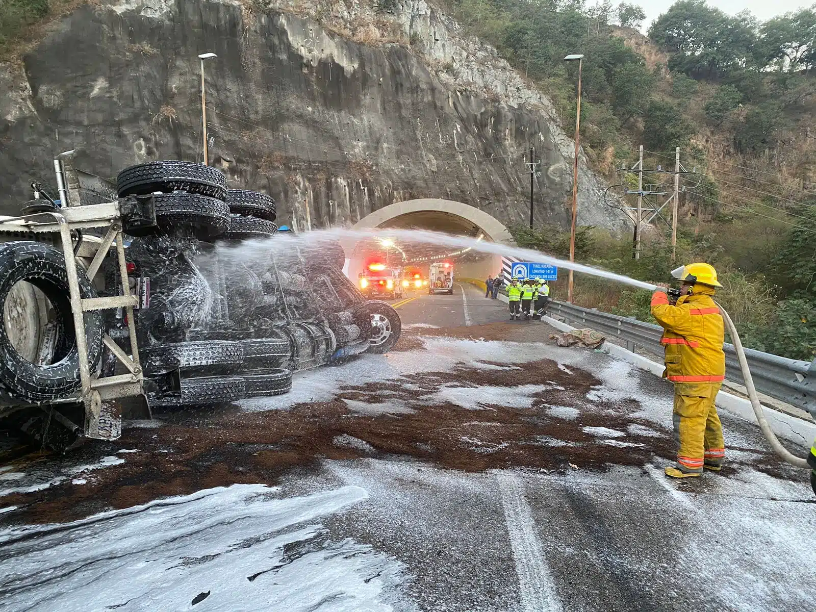Elemento de bomberos con una manguera con agua apagando el fuego de un remolque de un tráiler con gasolina en la autopista Durango-Mazatlán tras un accidente tipo volcadura