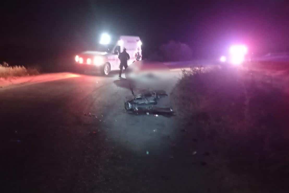 Motocicleta tirada en la carretera, a poca distancia un hombre tirado y una ambulancia