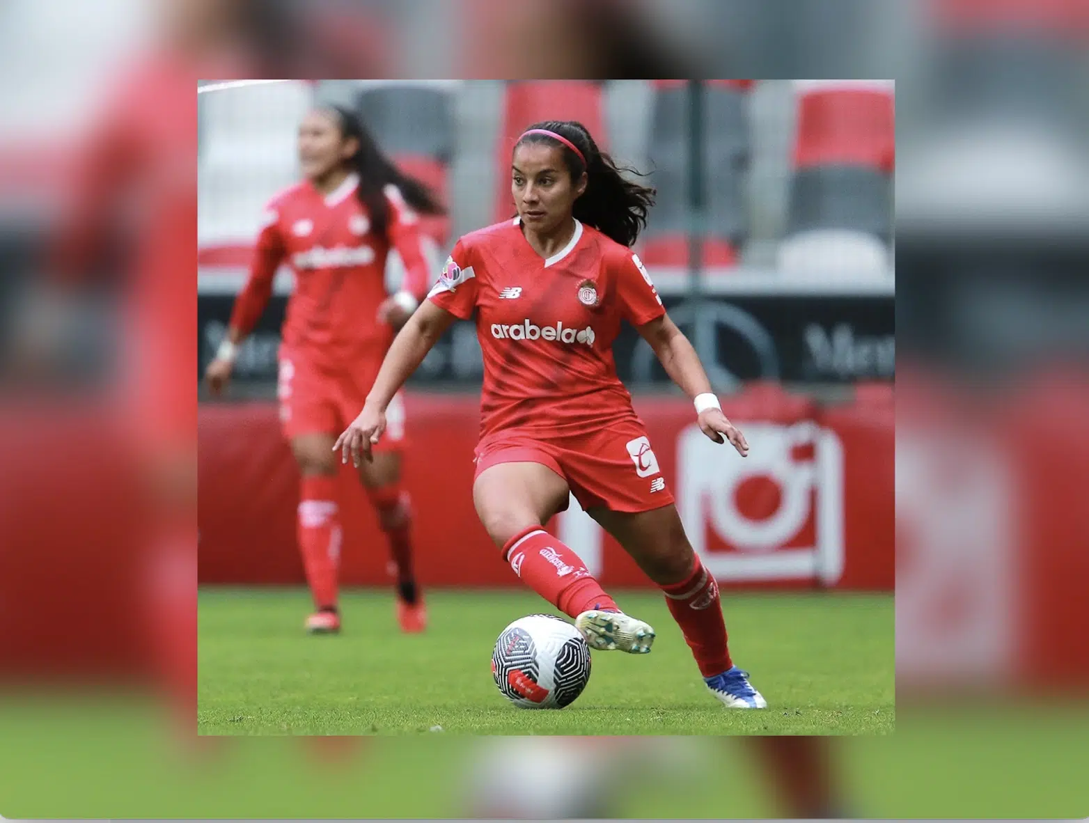 Cinthya Peraza con el uniforme del equipo de Toluca en una cancha y conduciendo un balón dude futbol