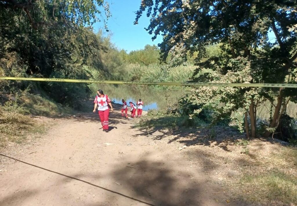 Elementos de la Cruz Roja en el lugar donde encontraron el cuerpo de un hombre sin vida en el río Sinaloa en Guasave y cinta amarilla delimitando el área
