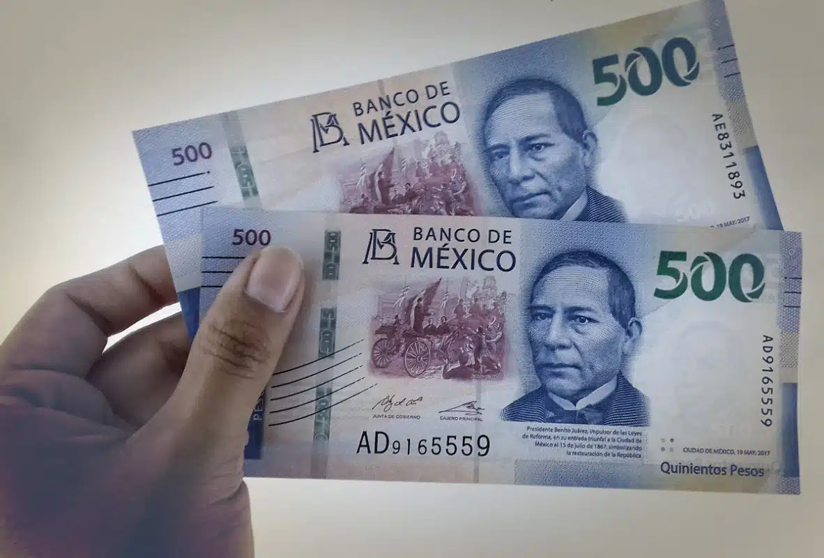 Una mano sosteniendo dos billetes de 500 pesos mexicanos