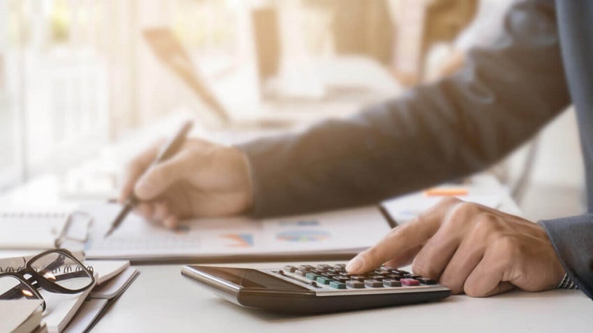 Persona sacando cuentas con una calculadora y escribiendo en unos documentos