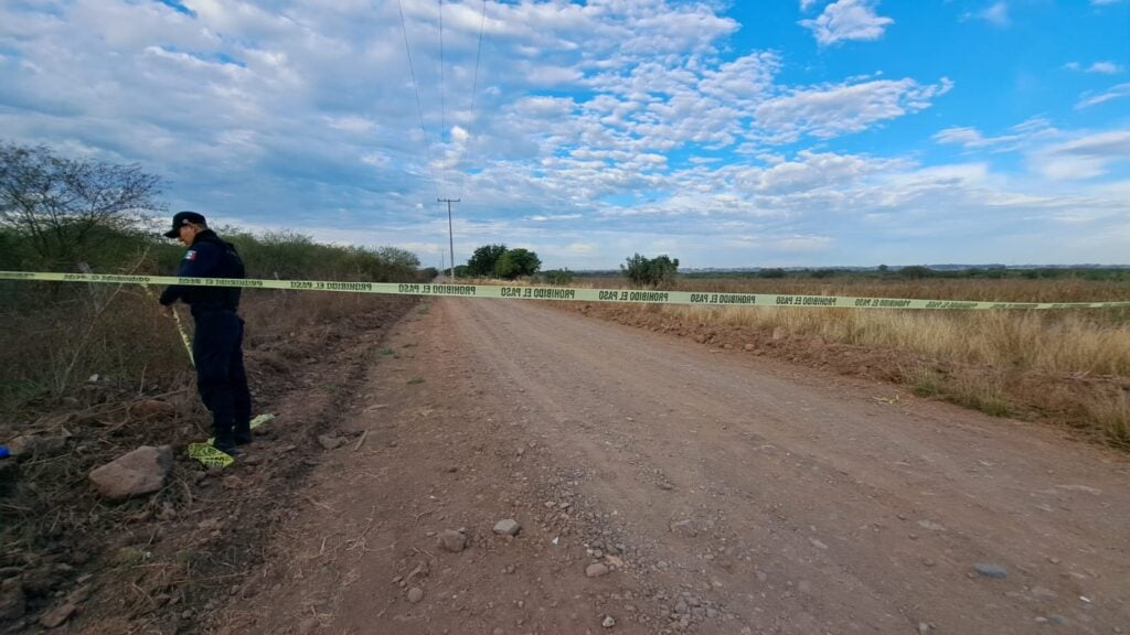 Policía en zona de terracería donde hay cinta amarilla por un homicidio 