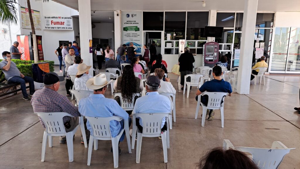 Personas sentadas esperando turno para pagar el impuesto del predial urbano en Guamúchil