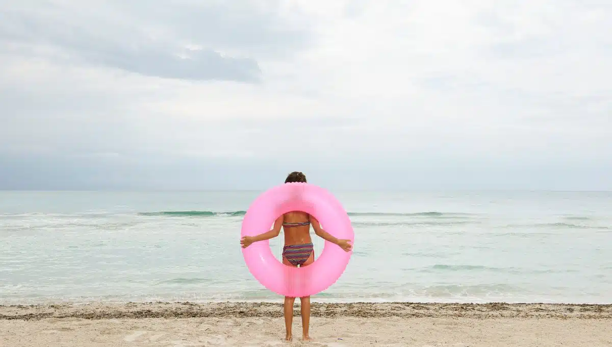 Mujer sosteniendo un inflable color rosa en la orilla de la playa