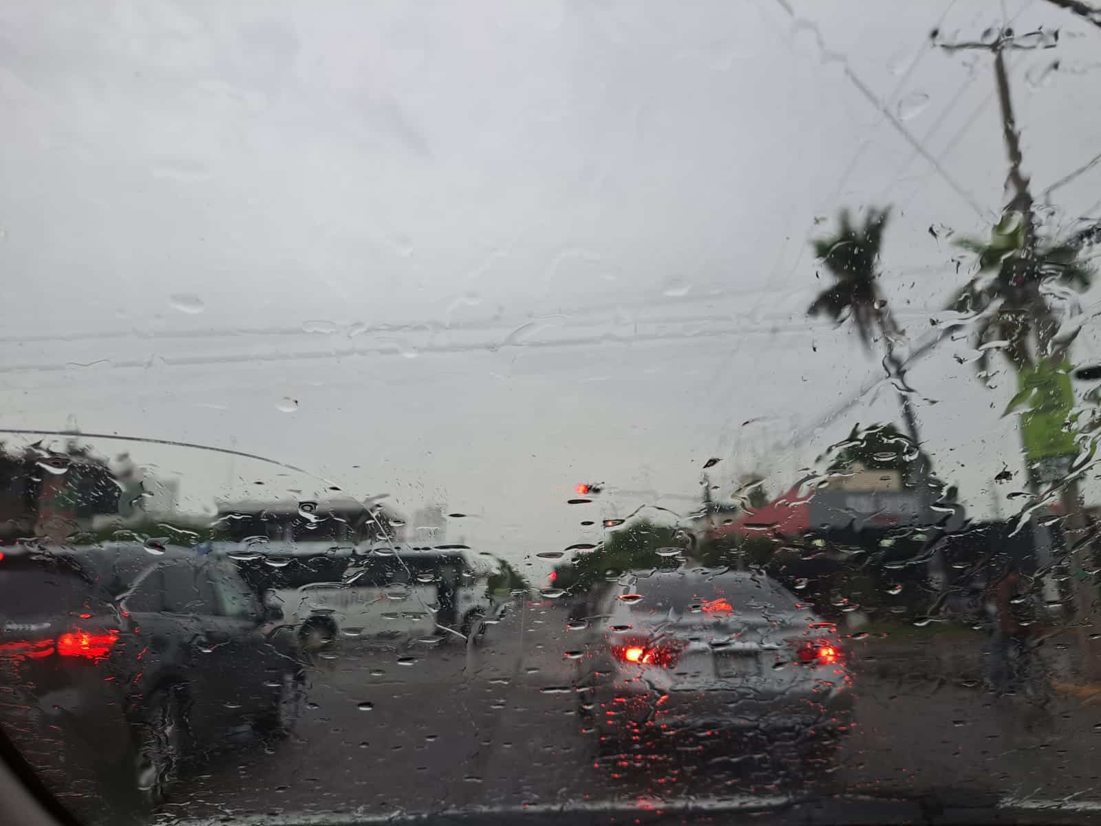 Gotas de lluvia en el cristal de un auto que va transitando por una avenida. Hay carros frente a este y el cielo se ve nublado