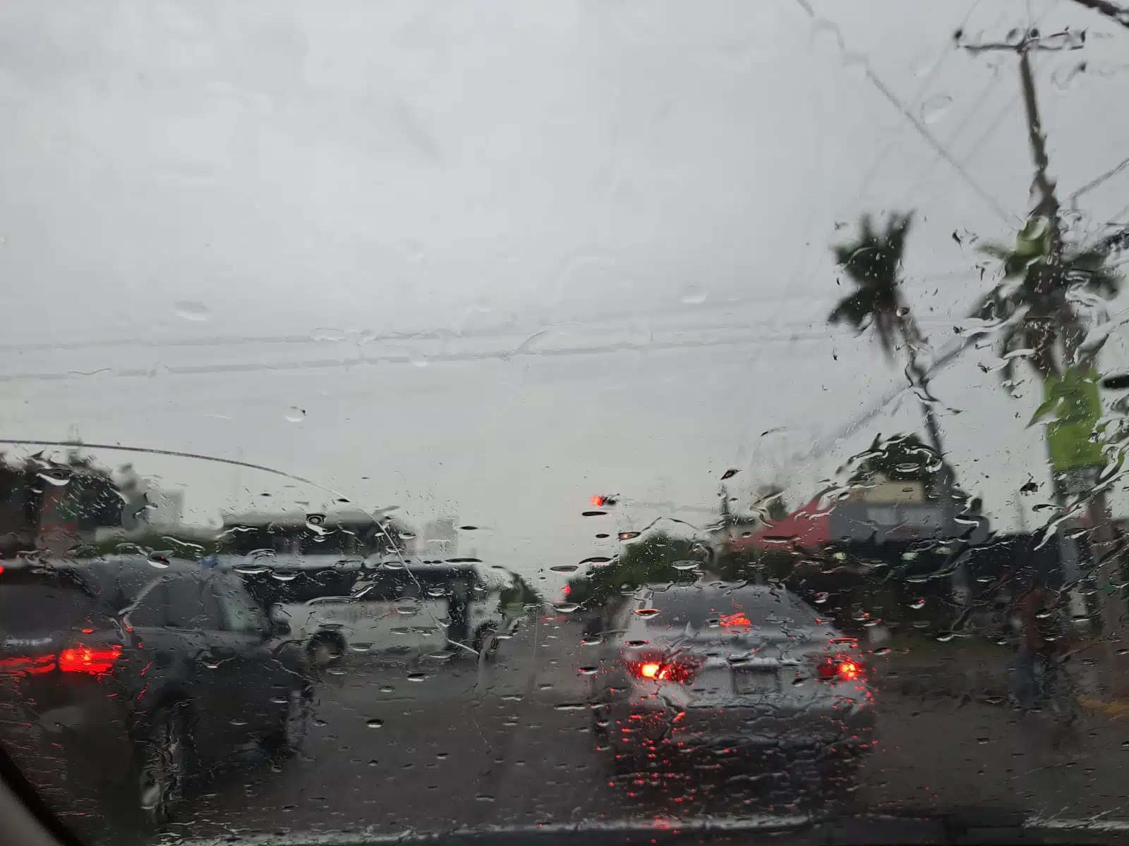 Gotas de lluvia en el cristal de un auto que va transitando por una avenida. Hay carros frente a este y el cielo se ve nublado