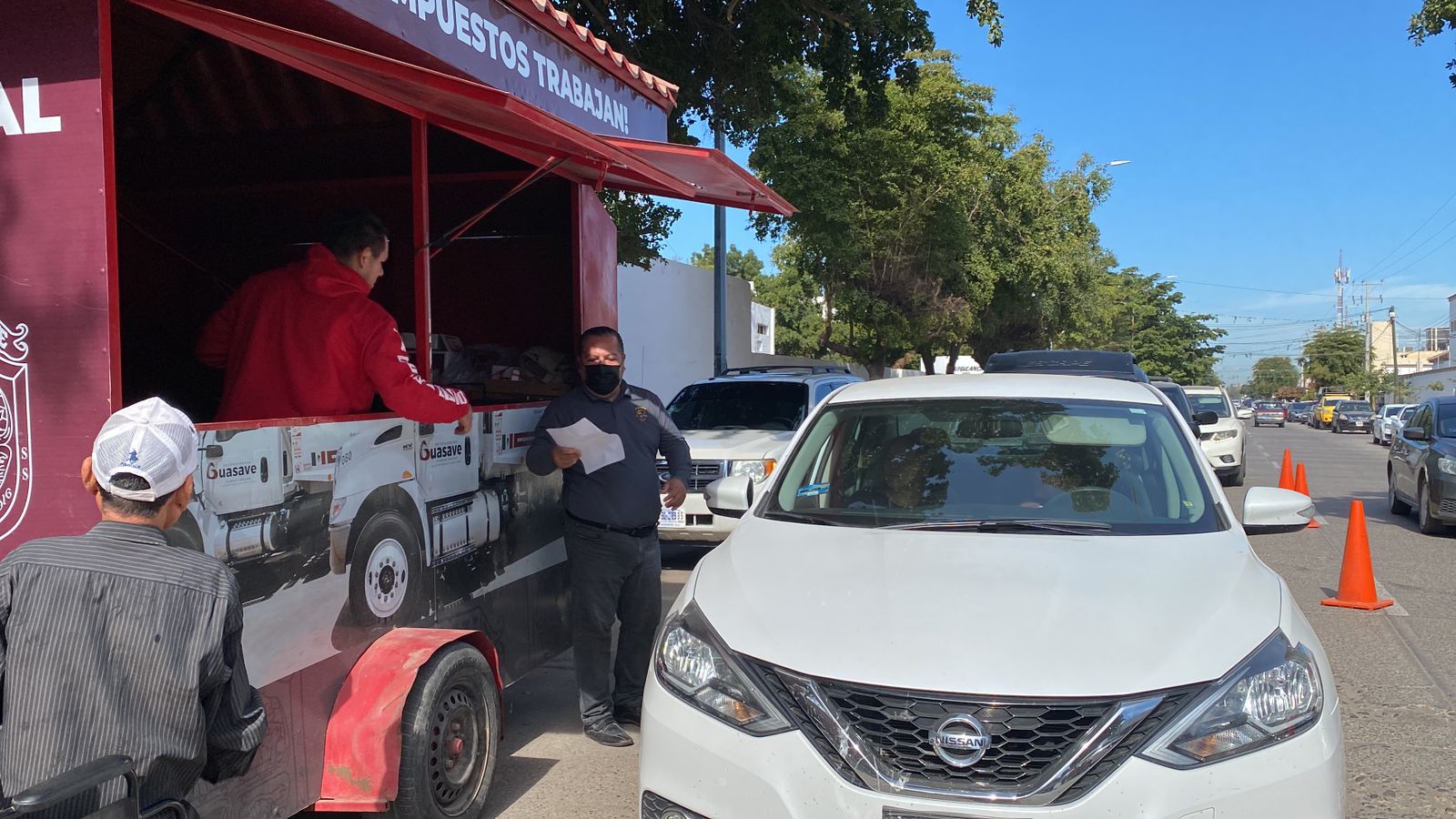 Un carro y una persona en un módulo móvil de pago para le predial de Guasave