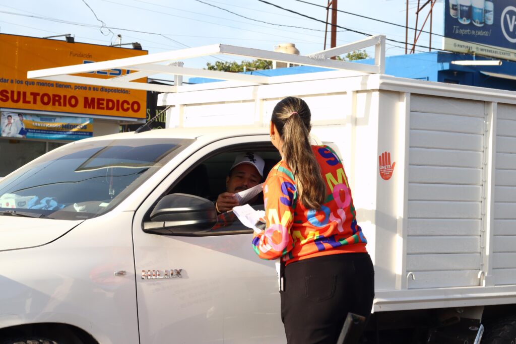 Mujer entregando un volante, sobre la violencia en contra de las mujeres, a un hombre de una camioneta en Los Mochis