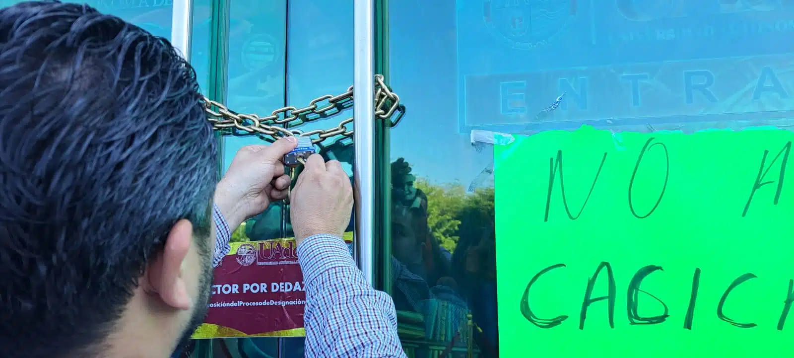 Las manos de una persona abriendo el candado de rectoría de la UAdeO en Culiacán