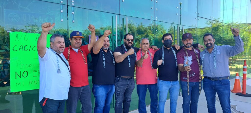 Trabajadores de la UAdeO con las cadenas en el cuello y una mano arriba en señal de que liberaron rectoría en Culiacán