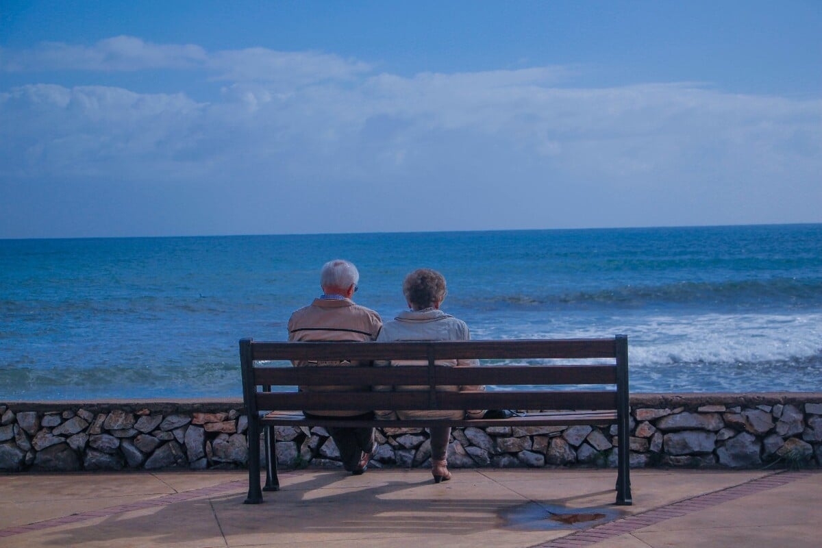 Pareja de adultos mayores sentados en una banca con vista al mar