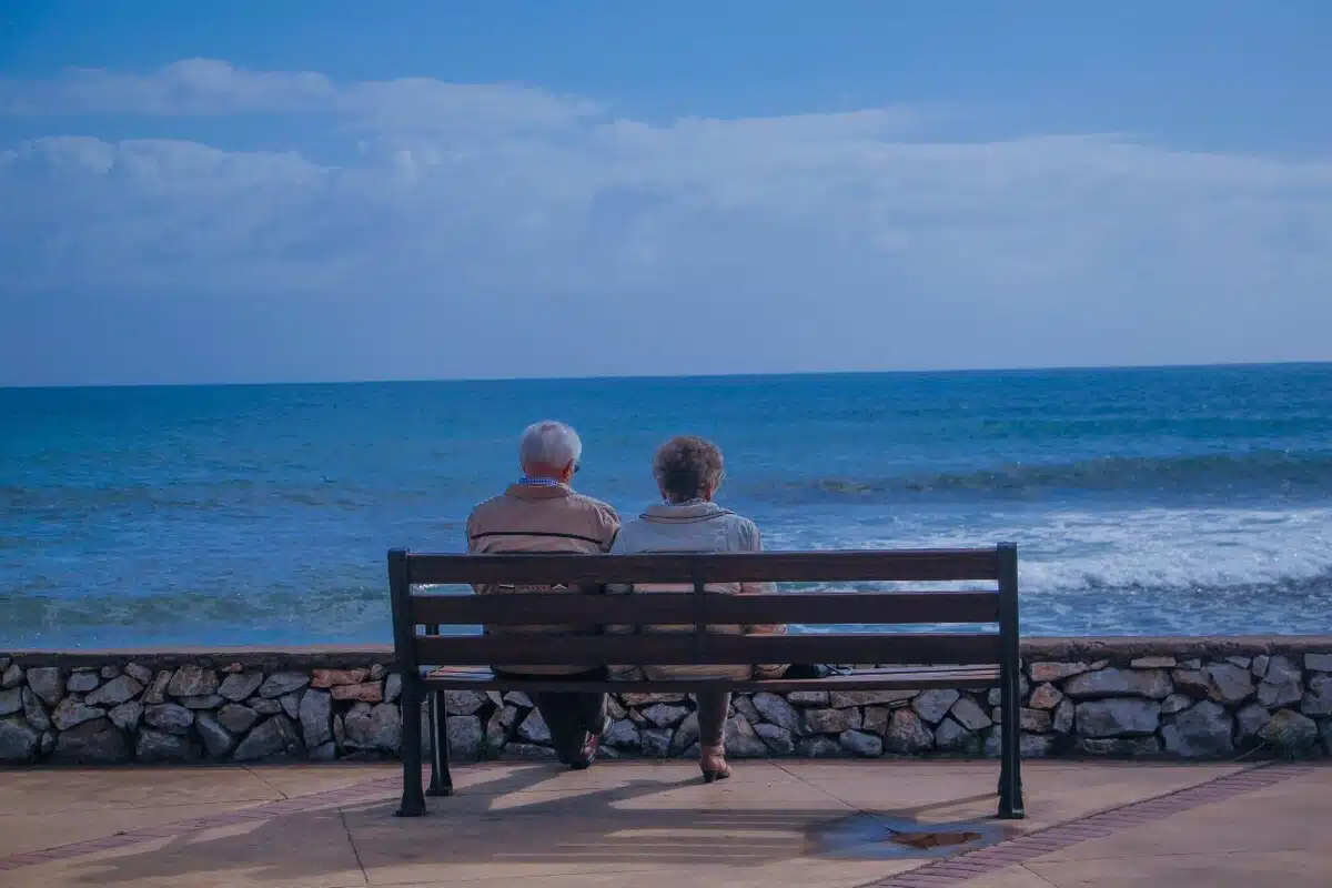 Pareja de adultos mayores sentados en una banca con vista al mar