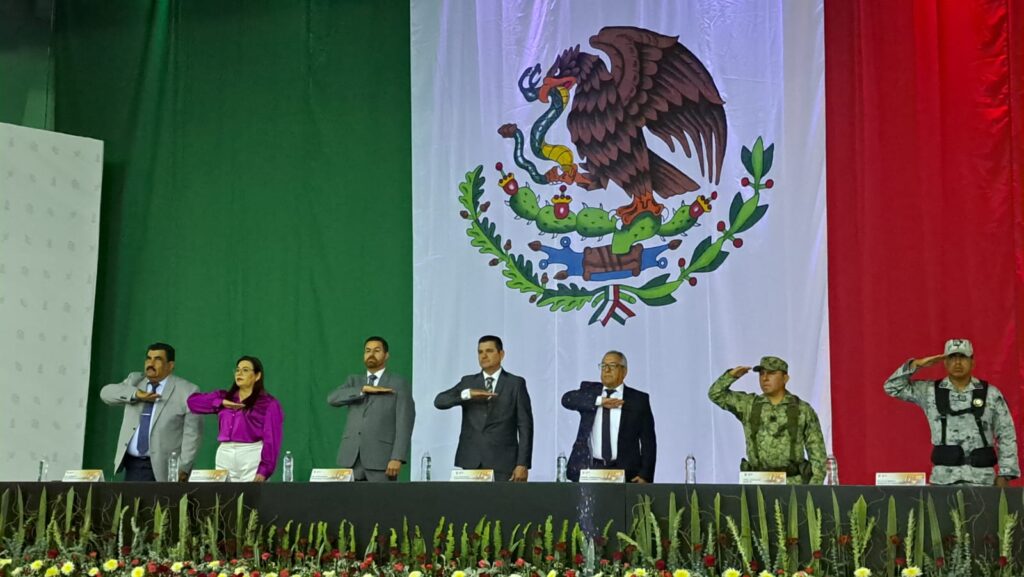 Bandera de México al fondo y diferente personalidades en la mesa del presidium en el 62 aniversario de Salvador Alvarado