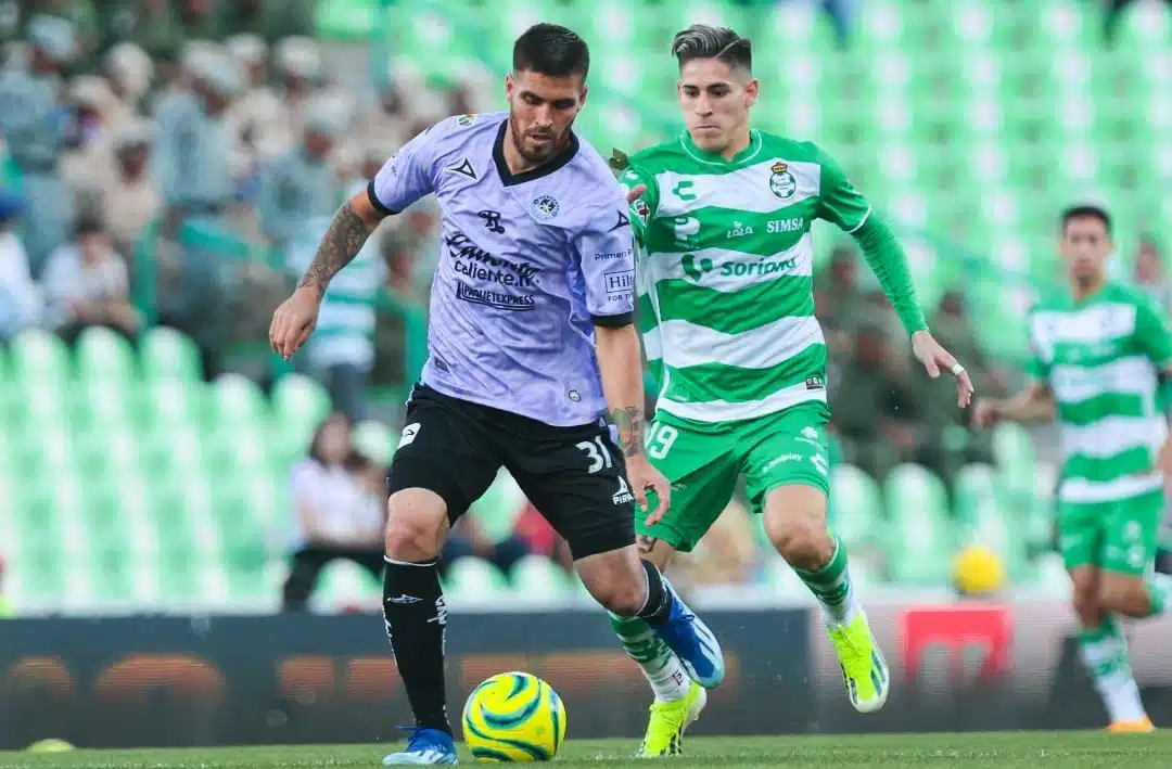 2 jugadores uno de Mazatlán FC y otro de Santos Laguna en una cancha de futbol disputándose un balón