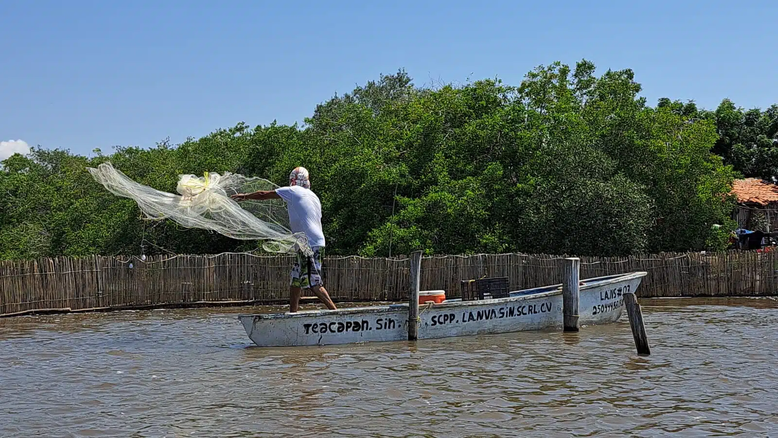 Pescador de El Ostial lanzando una red arriba de una panga en el mar