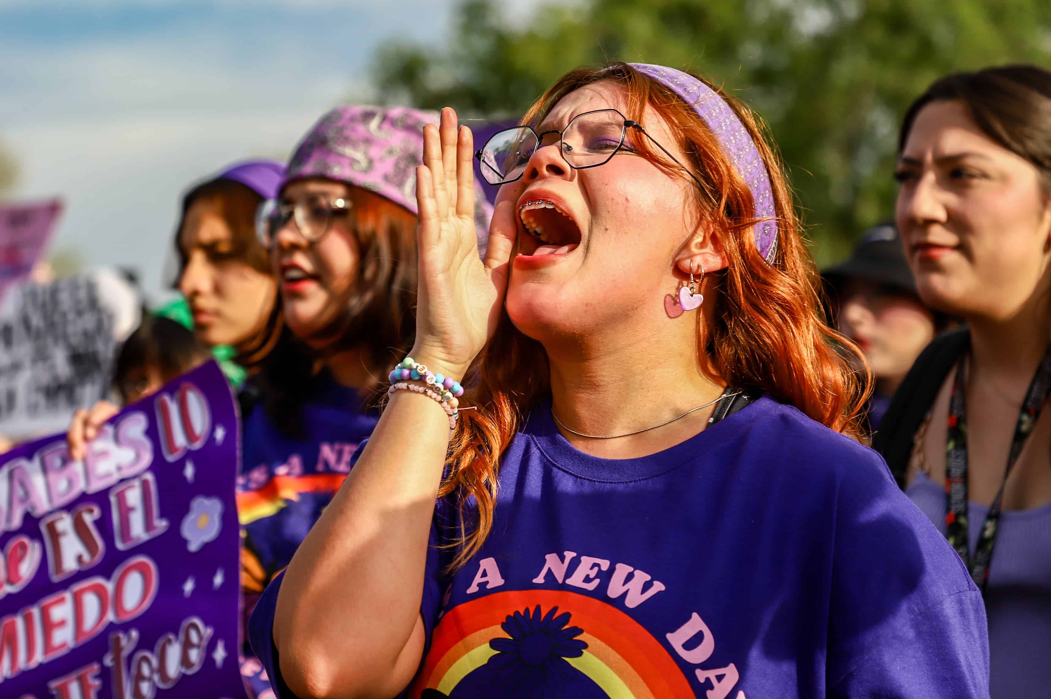 Jóvenes mujeres vestidas de color morado marchando y gritando para exigir sus derechos