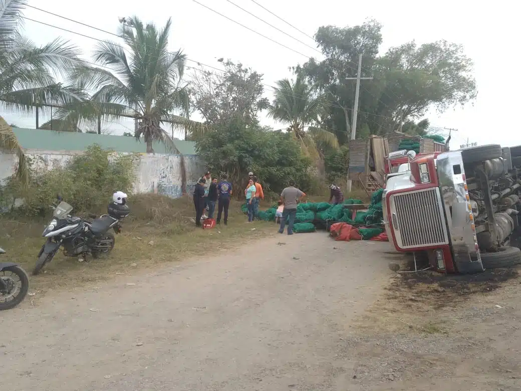 Personas en el lugar donde un tráiler tipo torton cargado de chiles terminó volcado sobre el lado del copiloto en Villa Unión