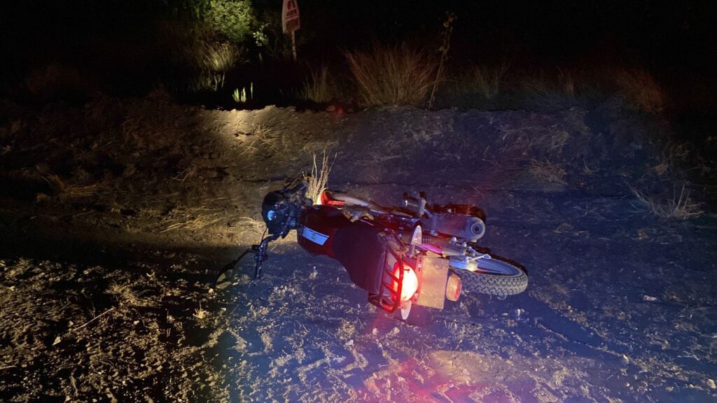 Motocicleta tirada en el suelo en una zona de terracería en medio de la obscuridad