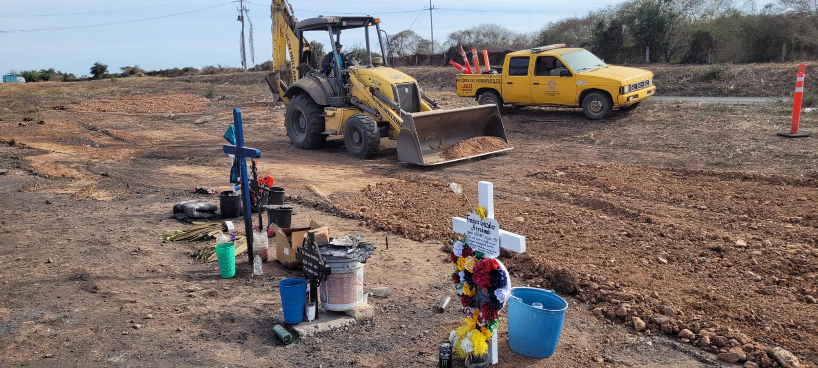 Retroexcavadora y camioneta de Protección Civil de Elota, cruces, baldes y flores en el lugar del accidente tipo incendio del autobús 502
