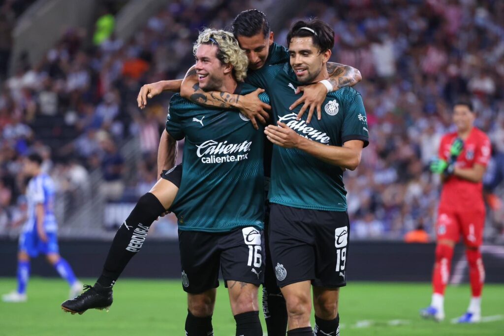 Cade Cowell, Carlos Cisneros y Ricardo Marín con el uniforme de futbol del equipo de Chivas del Guadalajara festejando un gol en el estadio de Monterrey