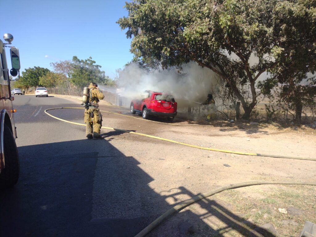 Elemento de Bombero con una manguera rociando de agua la camioneta que se incendio frente al Parque 87 en Culiacán