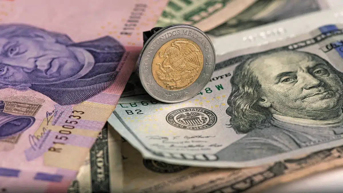 Moneda y billete mexicanos sobre un billete de 100 dólares