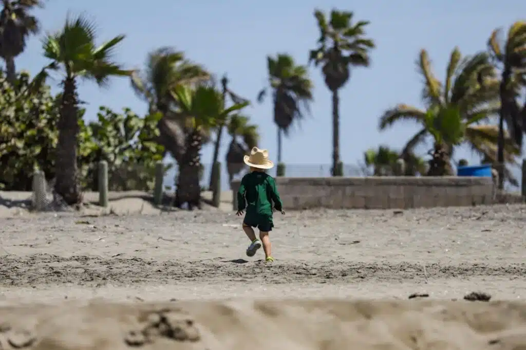 Niño de espaldas con un sombrero mientras camina sobre la arena en la playa