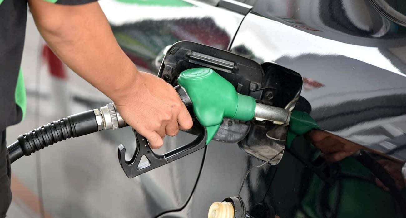 Mano de una persona sosteniendo la manguera de una bomba de gasolina mientras carga combustible a un vehículo