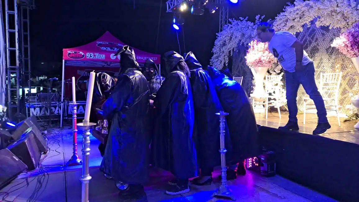 Personas cubiertos de pies a cabeza con traje negro arriba del escenario en el Carnaval de Guasave durante la Quema del mal humor