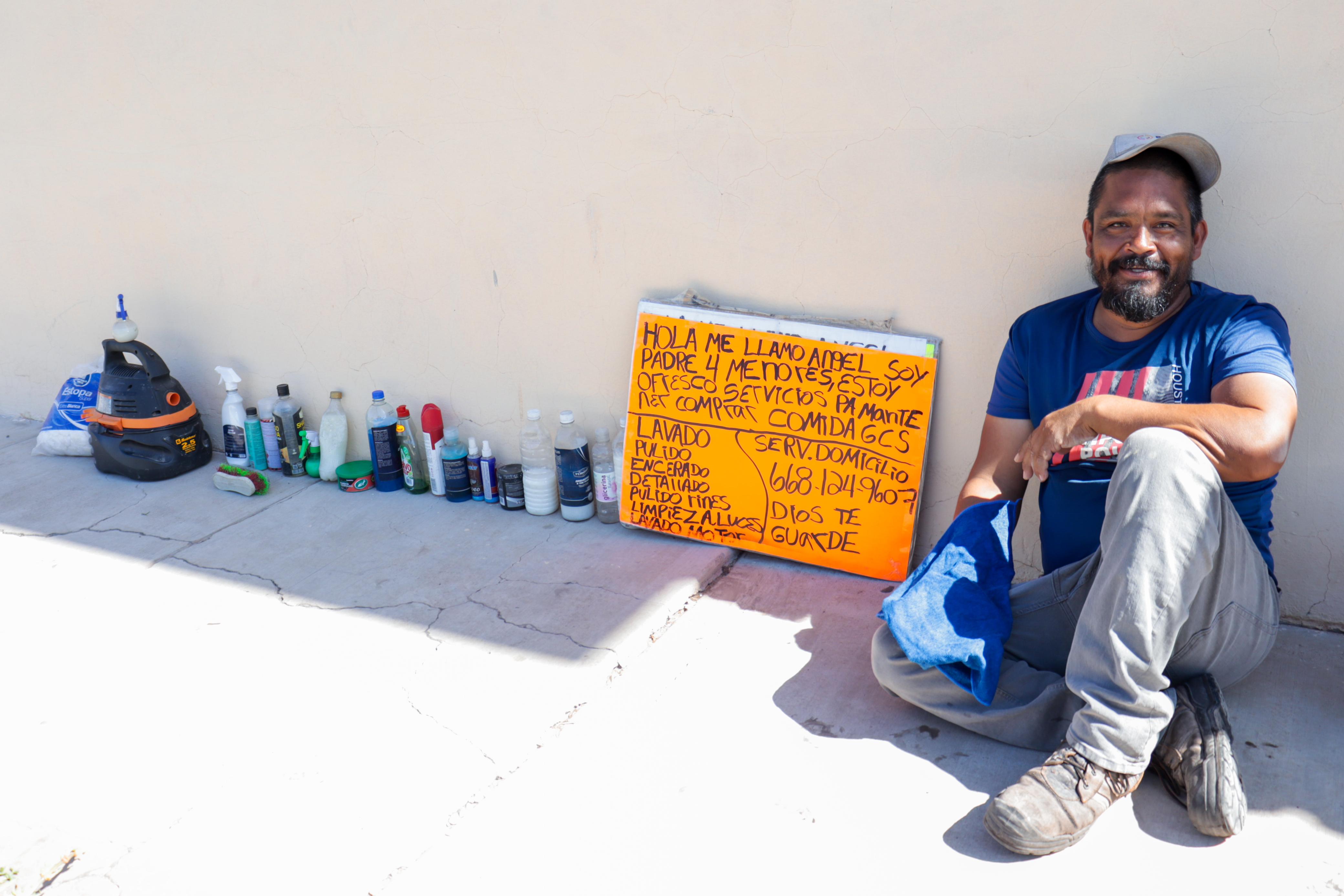 Hombre sonorense de complexión media sonriente y sentado en el suelo junto a productos de limpieza