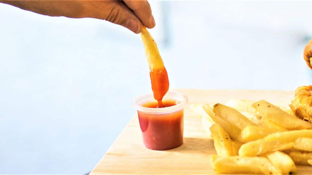 Una persona se sirve salsa catsup a una papa frita