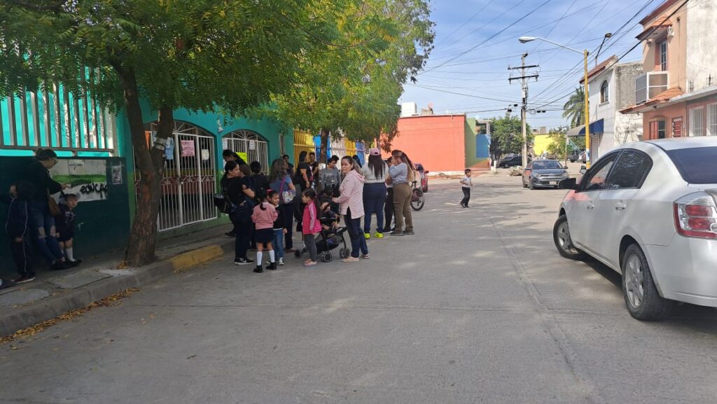 Padres de familia y niños en la entrada de un kínder que bloquean 