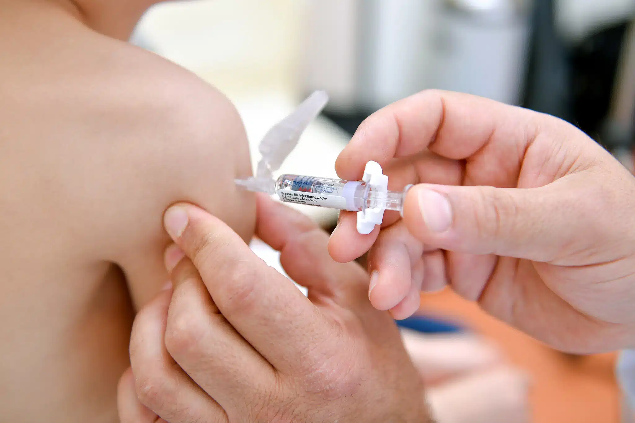 Manos de una persona vacunando en el brazo de un niño
