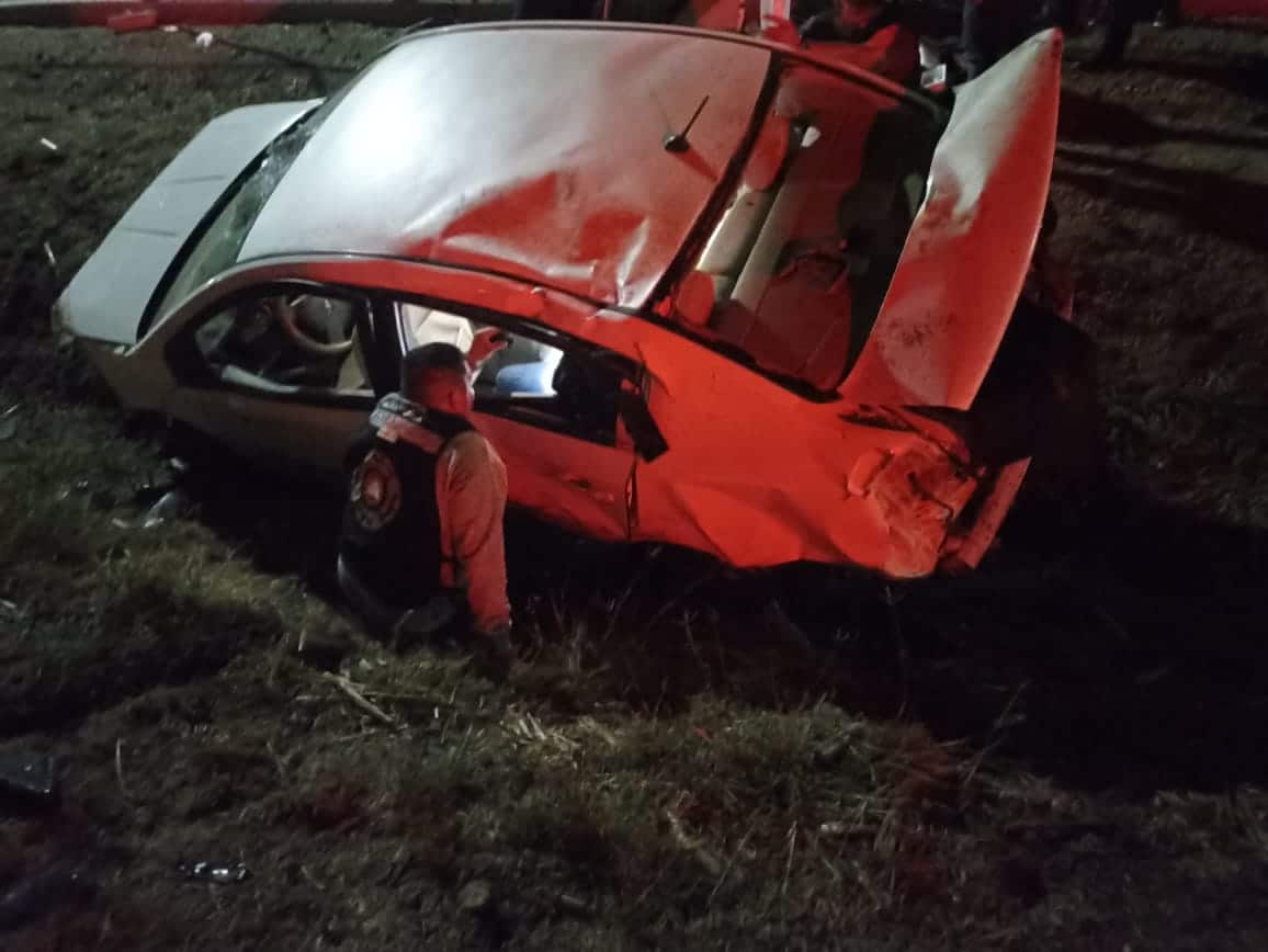 Camioneta en una zona de terracería tras volcar y una persona auxiliando a una mujer herida dentro del vehículo