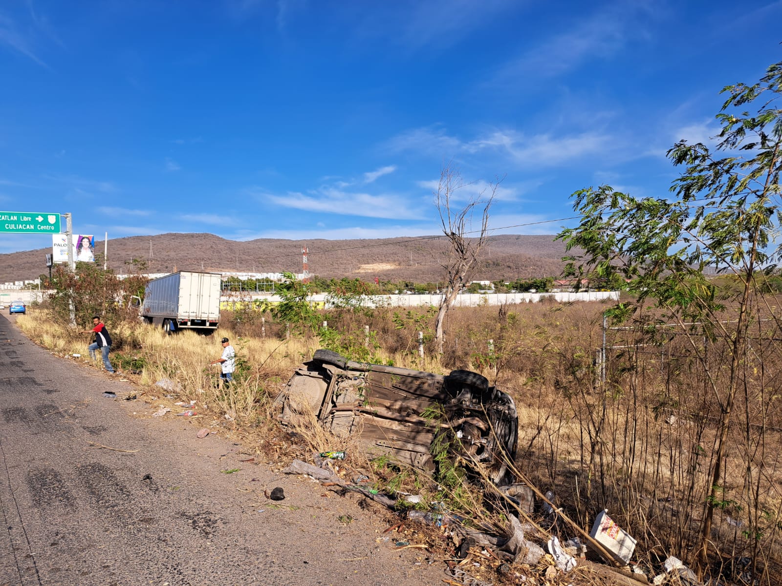 Un carro volcado con los neumático hacia arriba y un tráiler chocado al fondo tras un accidente por la Costera en Culiacán
