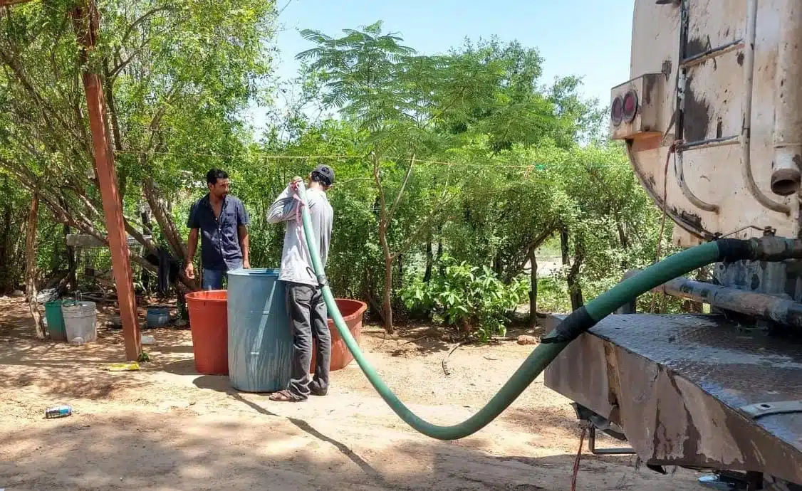 2 personas llenando unos tambos con agua de una pipa en El Fuerte