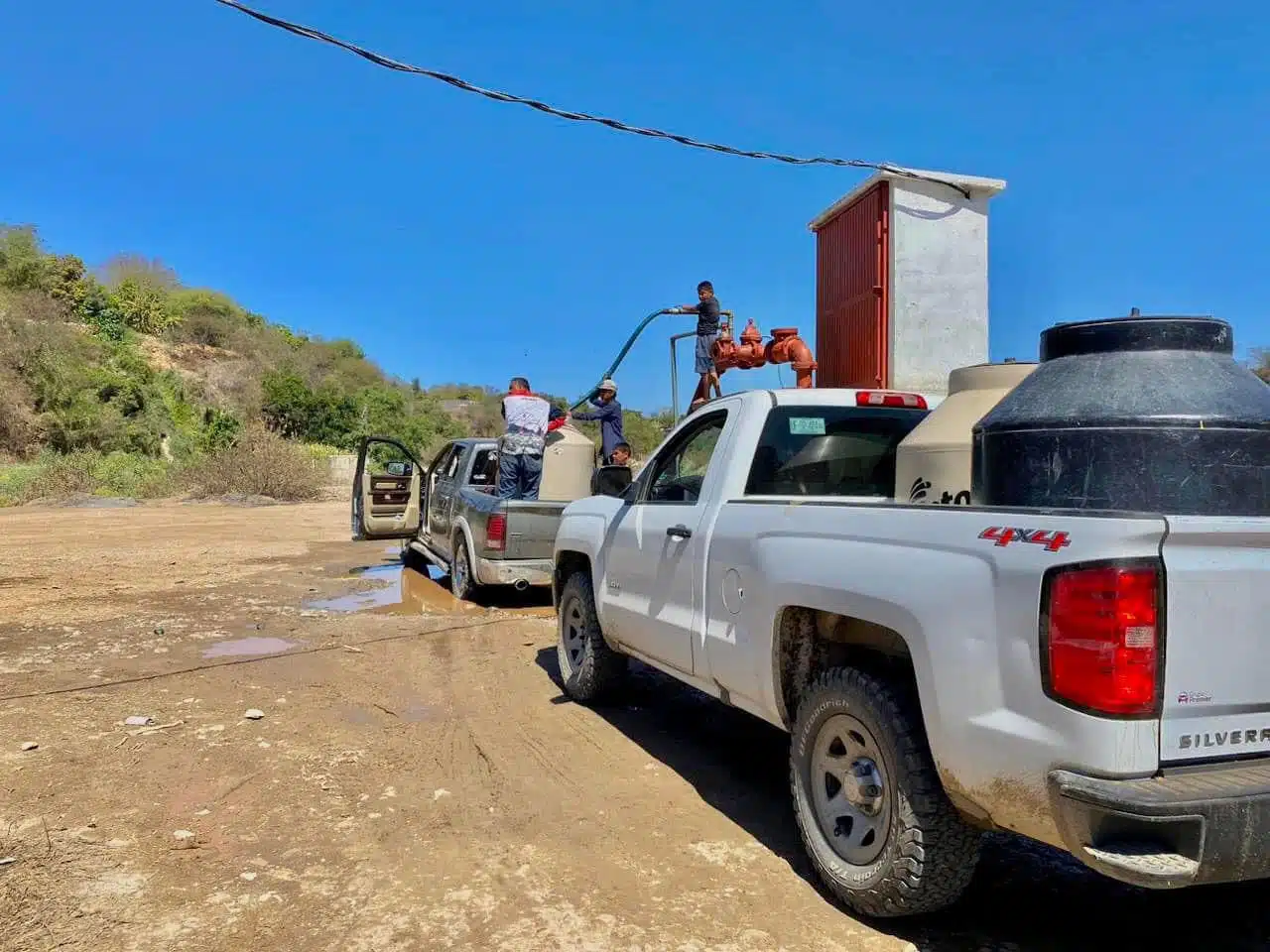 4 personas, 3 de ellas echándole agua a un tinaco que está arriba de una camioneta ante la sequía en Choix