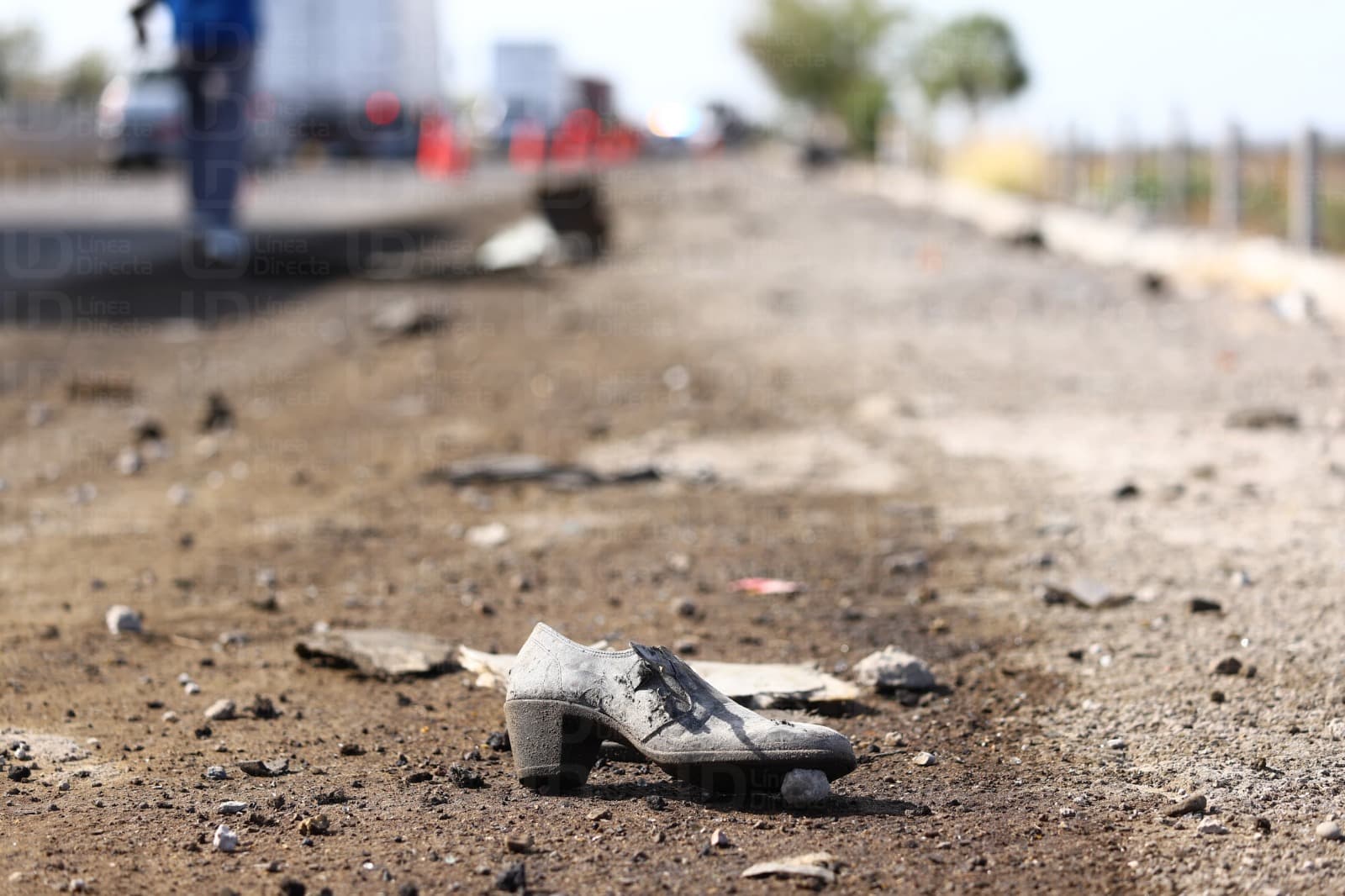 Zapato enfocado en medio del acotamiento de una carretera y al fondo policías en la zona de un accidente de camión