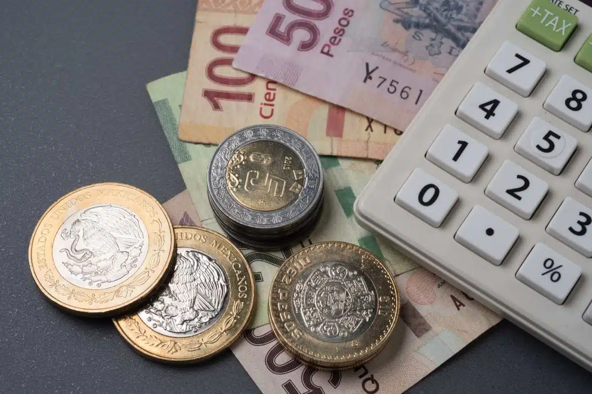 Monedas y billetes de pesos mexicanos junto a una calculadora
