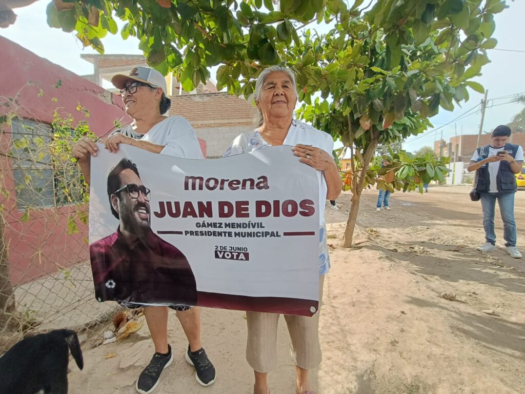 Mujeres sostienen cartel de Juan de Dios Gámez en Aguaruto