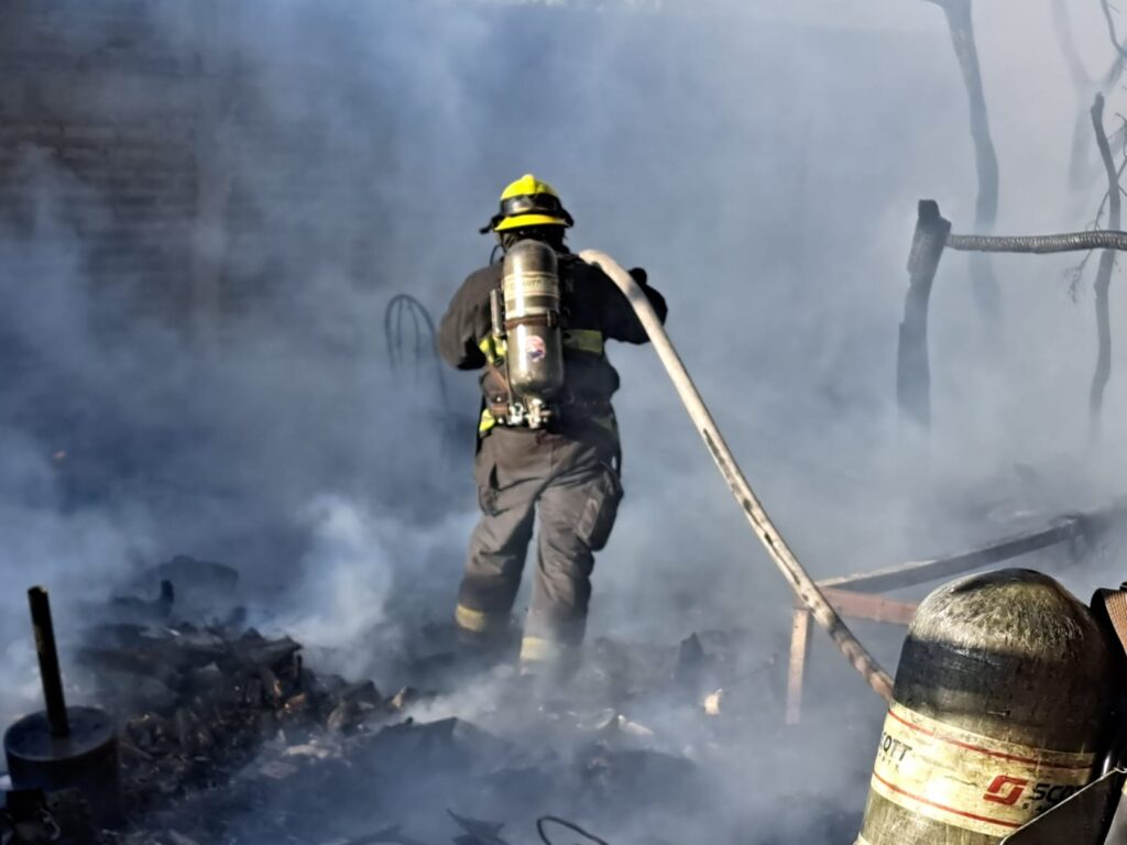 Elemento de Bomberos con una manguera apagando el incendio de una casa de madera en Culiacán