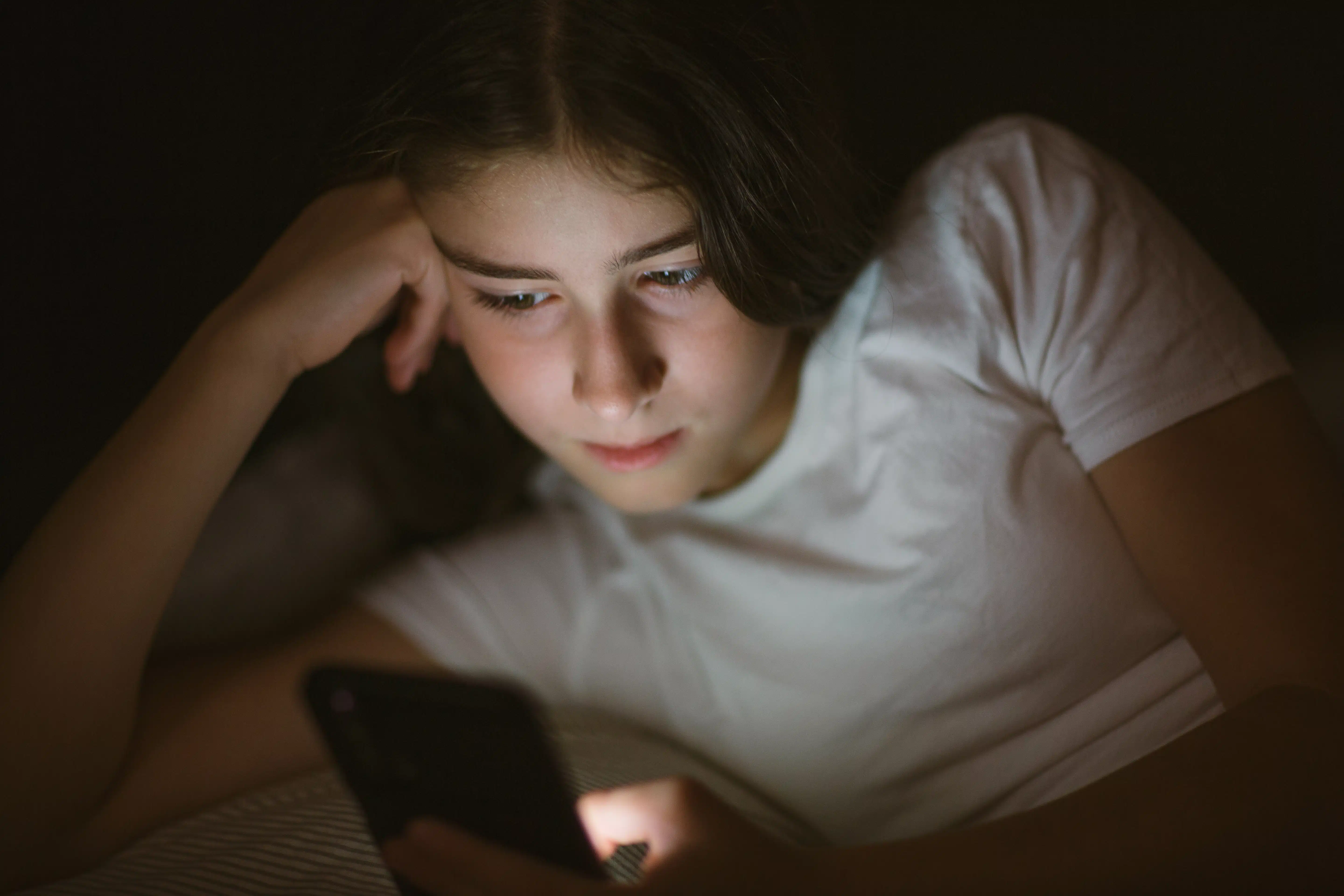 Adolescente viendo el celular en la cama por la noche