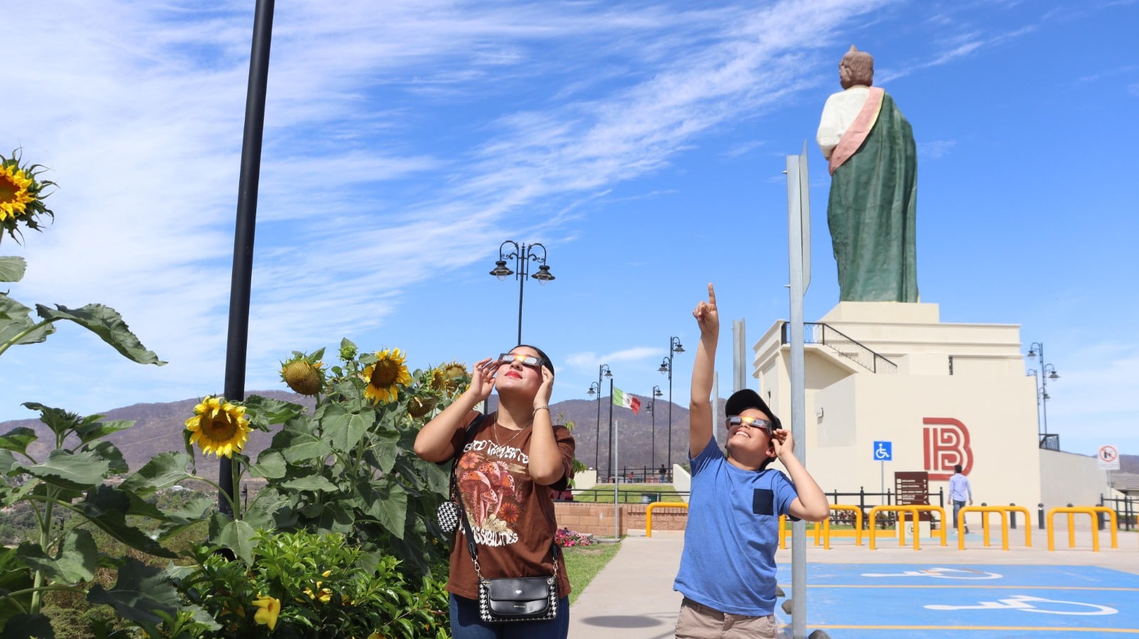 Personas en el parque Mirador de Badiraguato junto a San Judas Tadeo volteando al cielo para apreciar el eclipse total de Sol