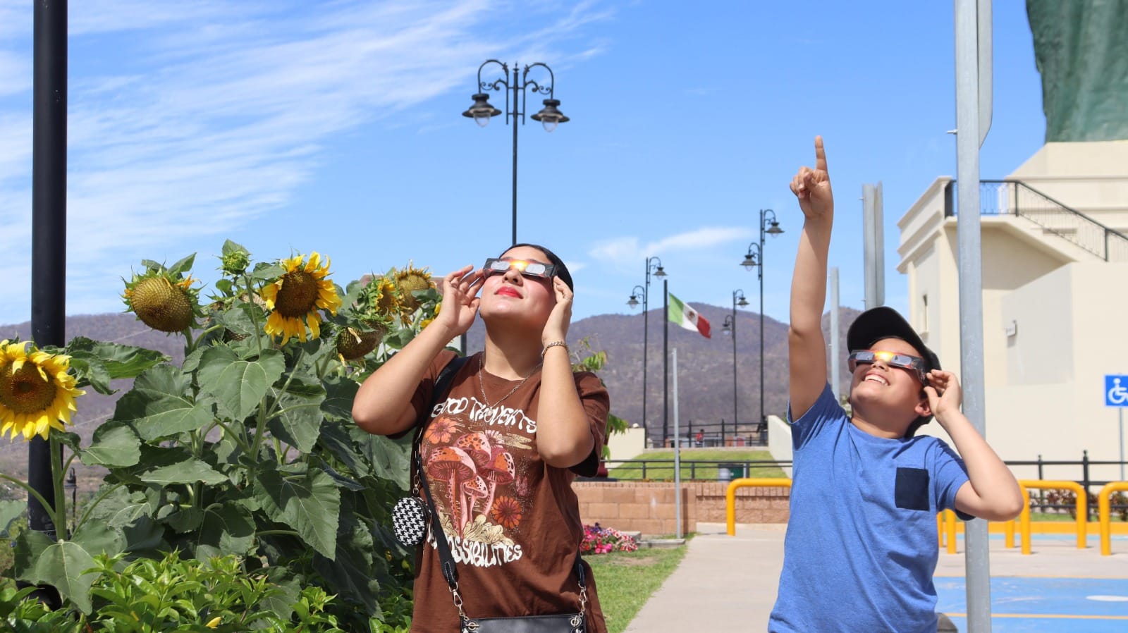 Personas en el parque Mirador de Badiraguato junto a San Judas Tadeo volteando al cielo para apreciar el eclipse total de Sol