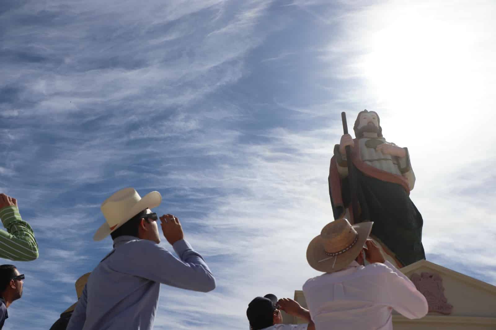 Personas en el parque Mirador de Badiraguato junto a San Judas Tadeo volteando al cielo para apreciar el eclipse total de Sol