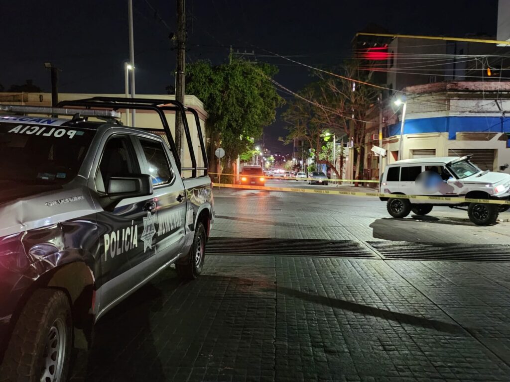 Cinta amarilla delimitando el área donde está una camioneta que manejaba un hombre que murió tras un presunto infarto y chocar contra una luminaria en Culiacán y una patrulla de la Policía Municipal